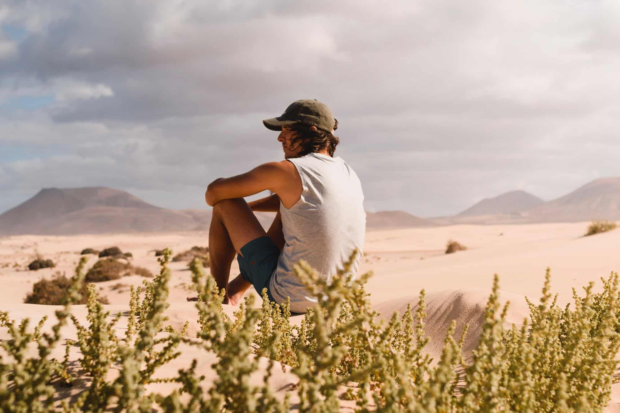 homme avec casquette assis sur le sable désertique des dunes de Corralejo à Fuerteventura