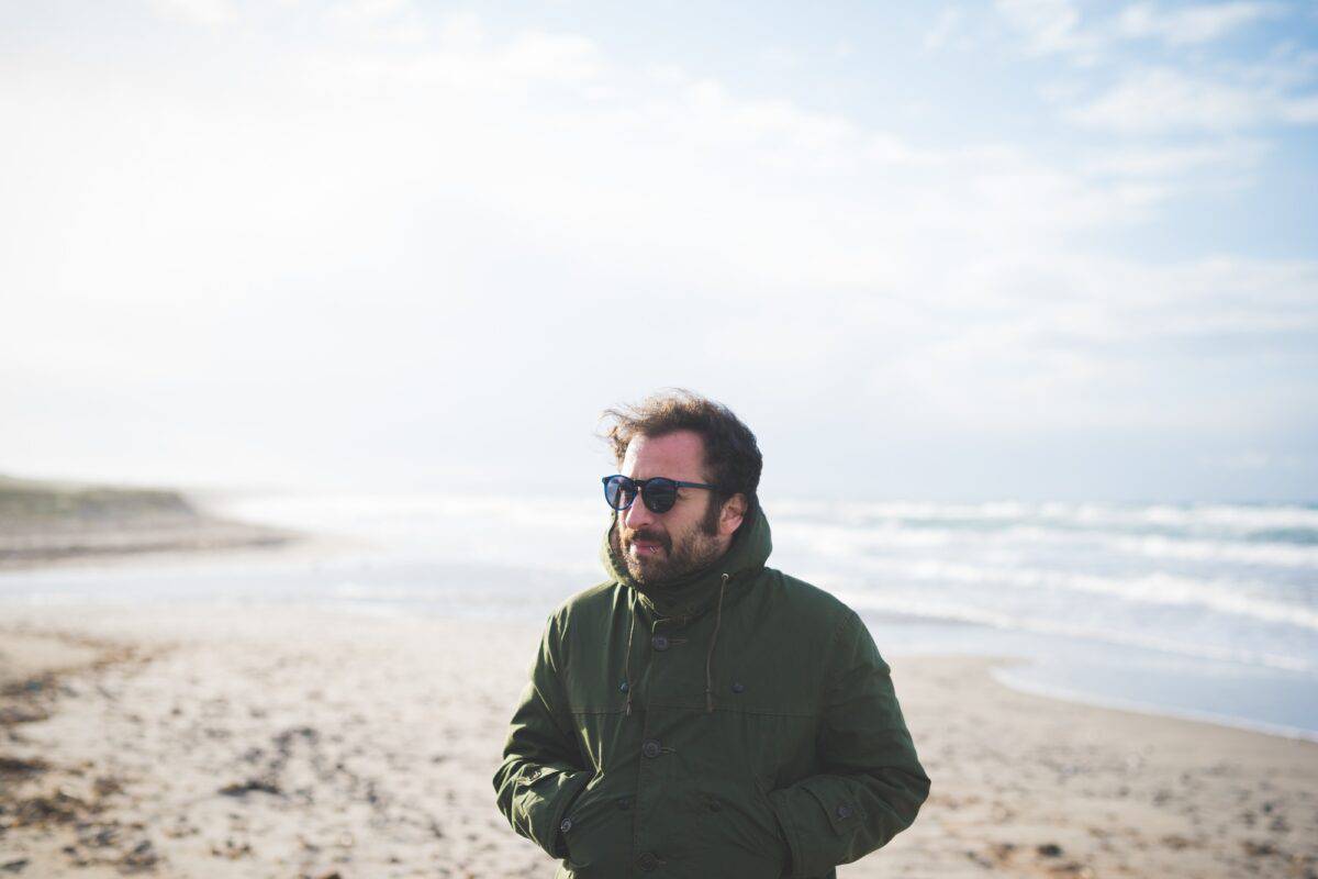 Mid adult man with hands in pocket on breezy beach, Sorso, Sassari, Sardinia, Italy